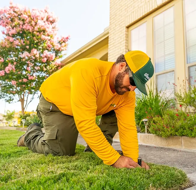 The Grounds Guys service professional adjusting a sprinkler head in the grass.