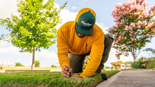The Grounds Guys service professional adjusting a sprinkler head in the grass.